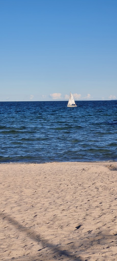 Segelboot auf der Ostsee, bewegte Wellen. Im Vordergrund Sandstrand.