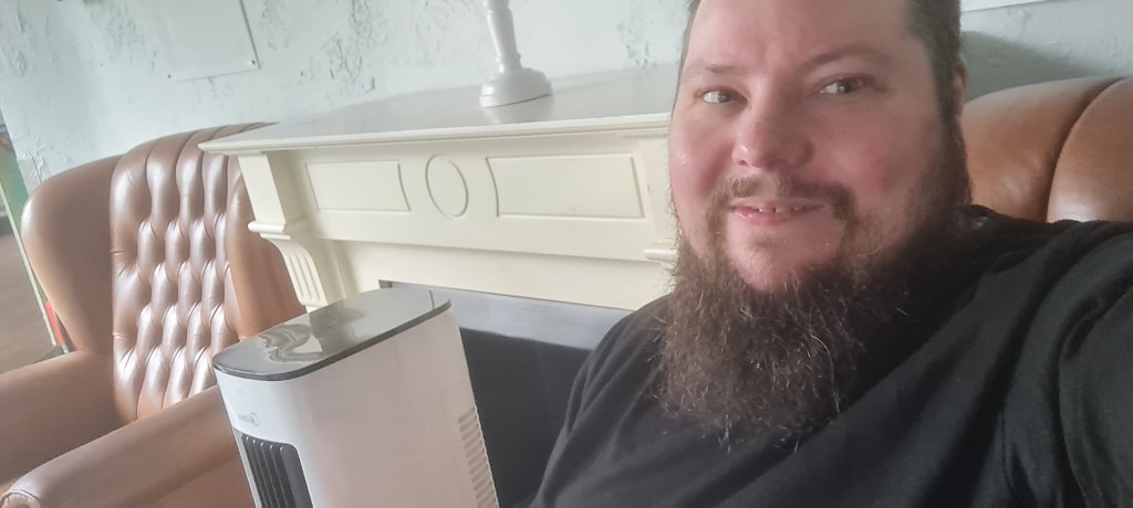 Mann mit Bart schaut in die Kamera. Im Hintergrund ist ein zweiter Ohrensessel zu sehen, der dem gleicht, auf dem der Mann sitzt.