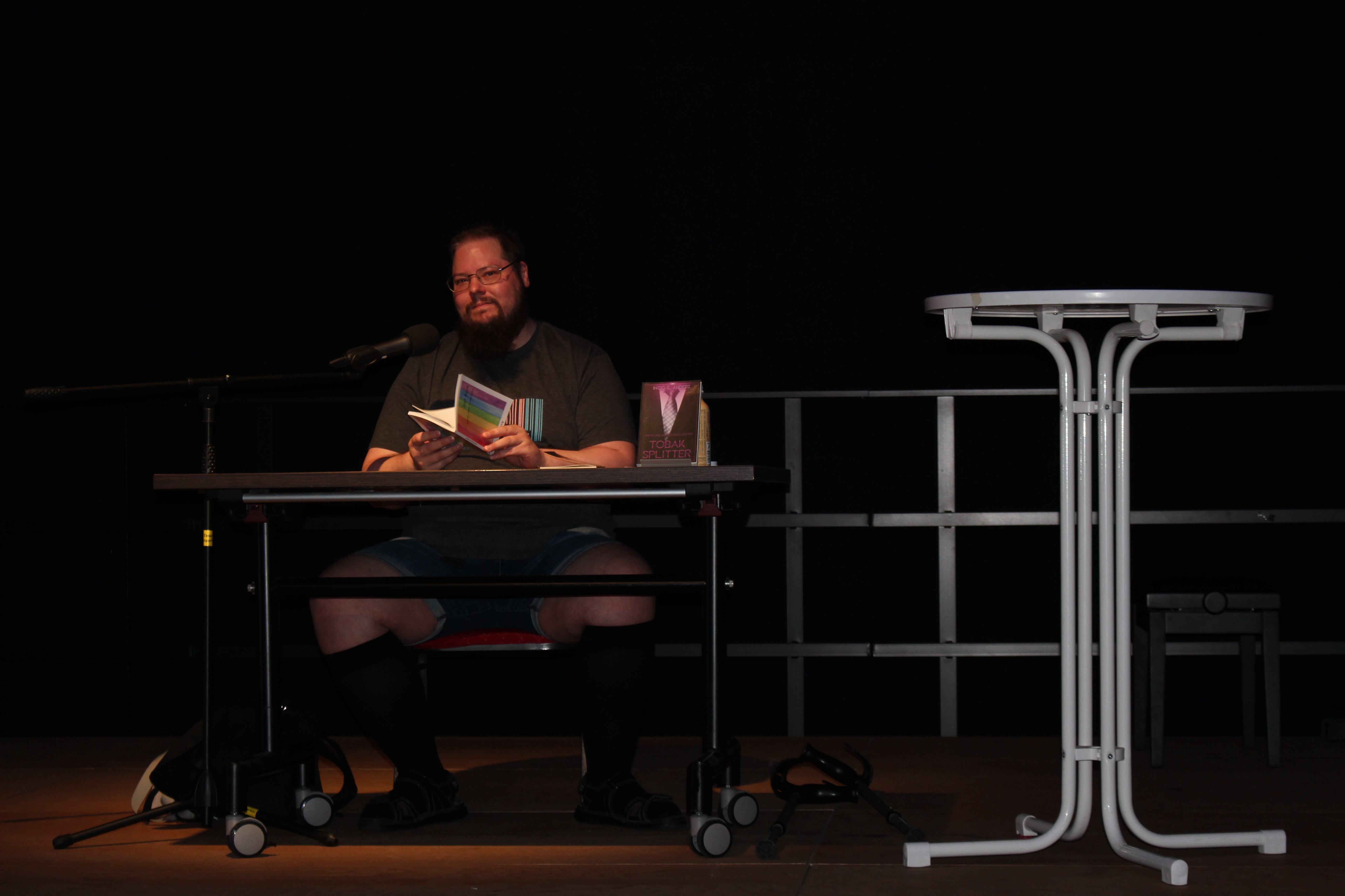 Ingo S. Anders sitzt auf der Bühne und liest. Just in diesem Moment schaut er ins Publikum.