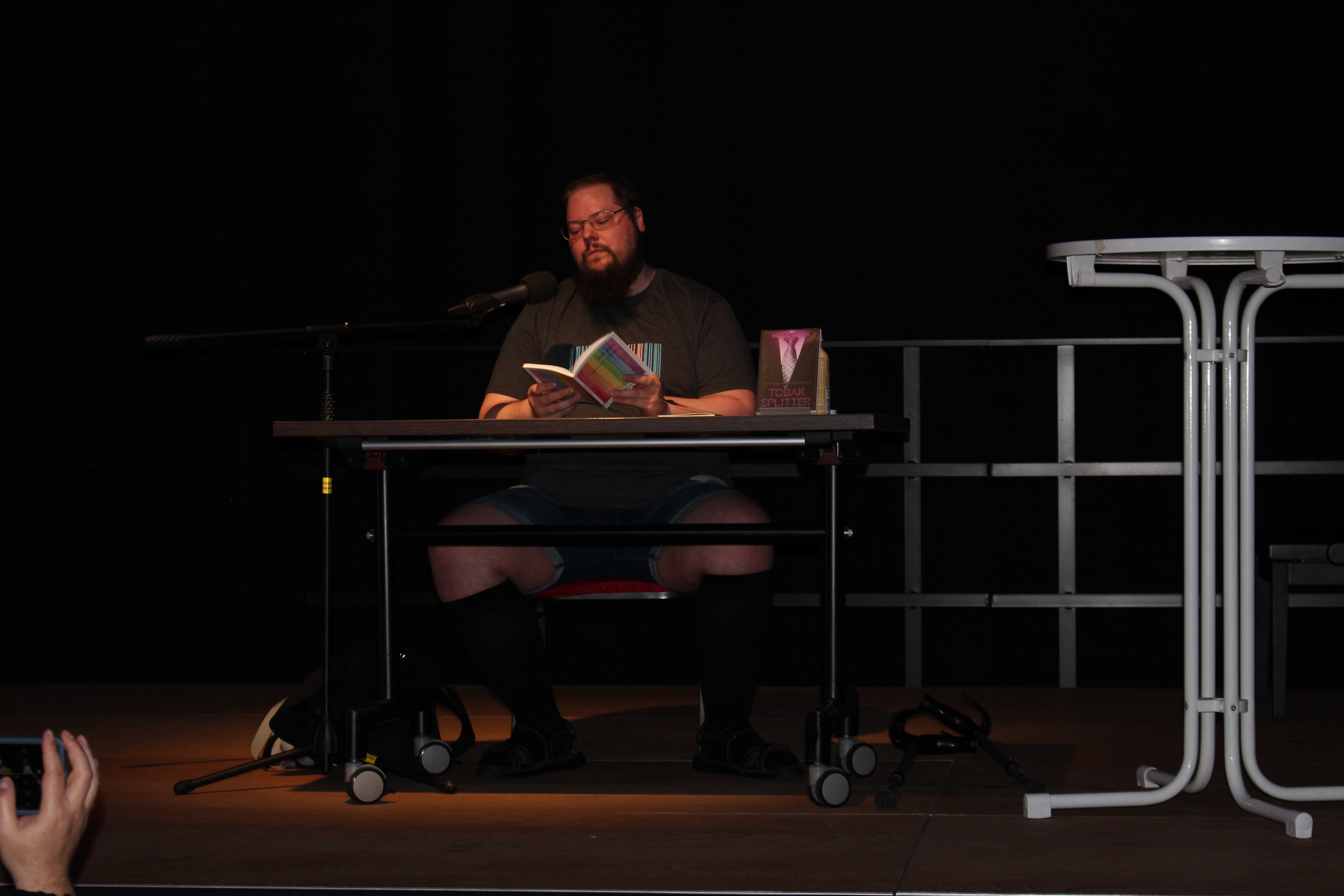 Ingo S. Anders sitzt auf der Bühne und liest. Er schaut in sein Buch.